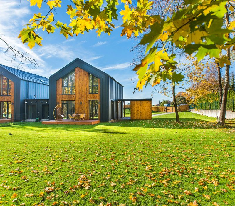 Contemporary wooden houses with lush green lawns surrounded by vibrant autumn foliage.